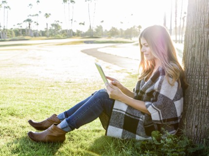 Hispanic woman leaning on tree using digital tablet