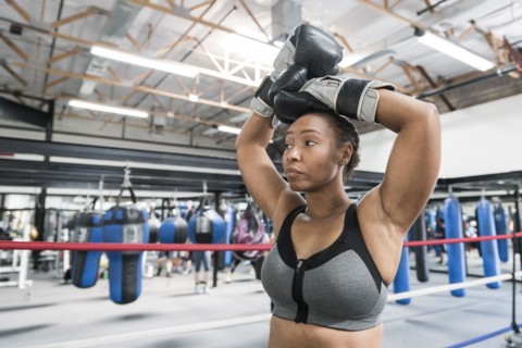 Black woman resting with arms raised in boxing ring