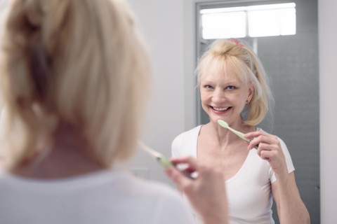 Caucasian woman brushing teeth in mirror