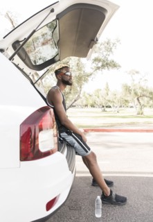 Black man sitting on car hatchback