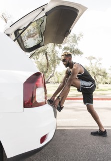 Black man leaning on car hatchback stretching leg