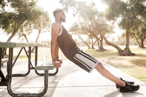 Black man leaning on picnic table in park stretching legs