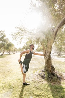 Black man leaning on tree in park stretching leg