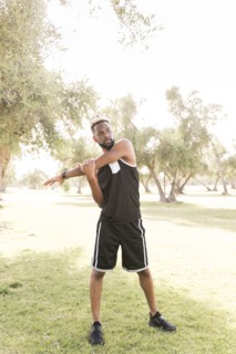 Black man standing in park stretching arm