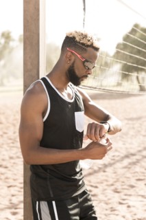 Black man leaning on beach volleyball net checking the time