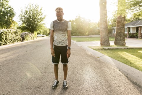Black man standing on street in the neighborhood looking down
