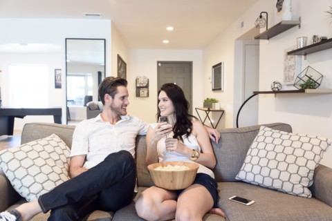 Smiling Caucasian couple relaxing on sofa with wine and popcorn