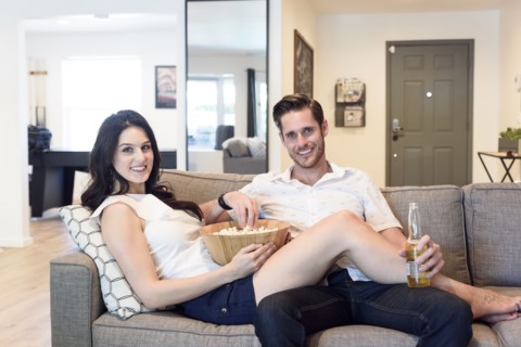 Smiling Caucasian couple relaxing on sofa with beer and popcorn