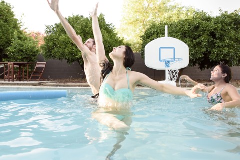 Caucasian friends playing basketball in swimming pool