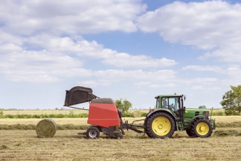 Caucasian man driving tractor baling hay