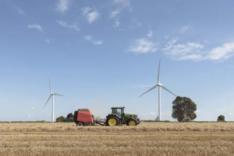 Caucasian man driving tractor near wind turbines