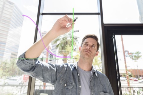 Caucasian man drawing diagram on glass wall