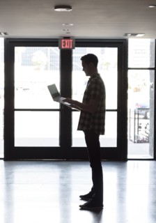 Caucasian man standing near doorway using laptop