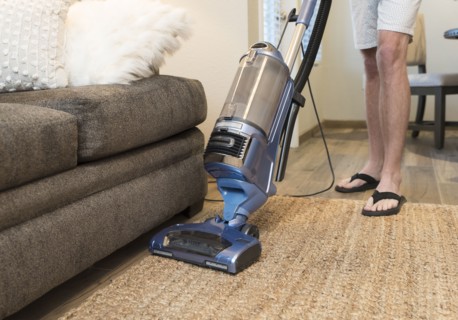 Legs of Caucasian man vacuuming rug near sofa
