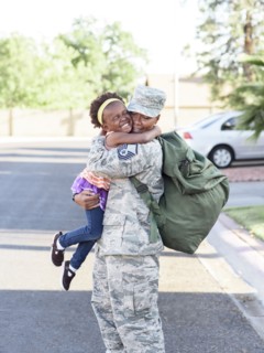 Black woman soldier hugging daughter in street