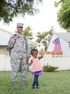 Smiling black woman soldier with daughter waving American flag