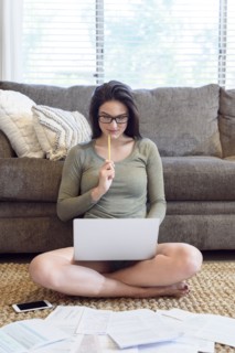Caucasian woman sitting on floor using laptop near paperwork