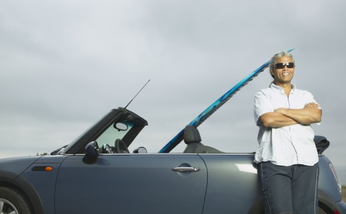 Senior man leaning on a convertible with a surfboard in it
