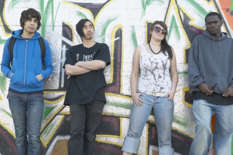 Group of young adults leaning against graffitied wall
