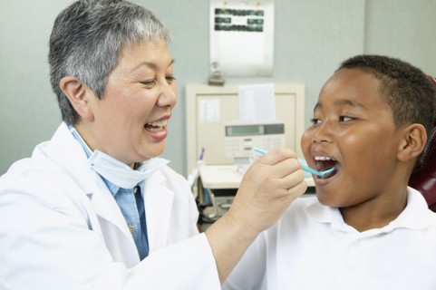 Senior Asian female dentist examining young male patient