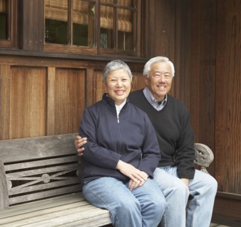 Senior Asian couple smiling and sitting on bench outdoors