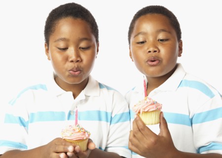 Young African twin brothers holding cupcakes with candles