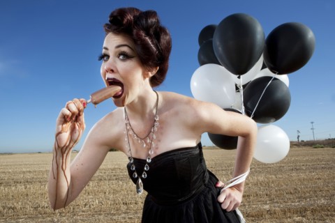 Glamorous woman holding balloons and eating popsicle