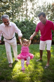 Father and grandfather helping daughter walk in backyard