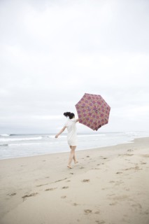 Woman walking in wind with umbrella on beach