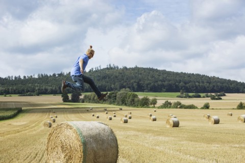 Farmer jumping over hay bale in field