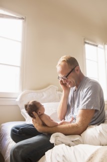 Father talking on cell phone and holding baby on bed