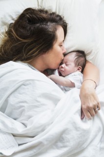 High angle view of mother kissing baby in bed