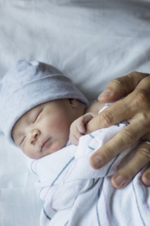 Close up of newborn baby holding finger of father