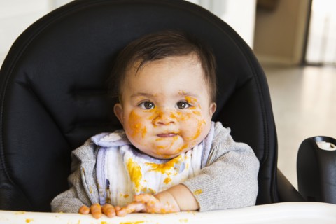Messy Mixed race baby eating food in high chair