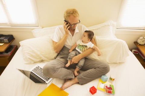 Father holding son and talking on cell phone on bed