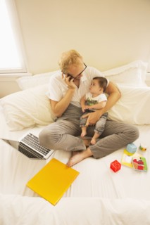 Father holding son and talking on cell phone on bed
