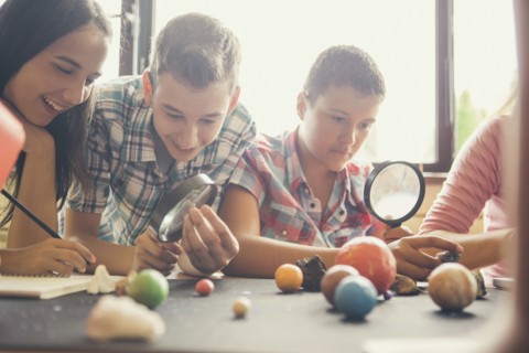 Students examining models of planets in classroom