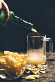 Hand pouring glass of beer near potato chips