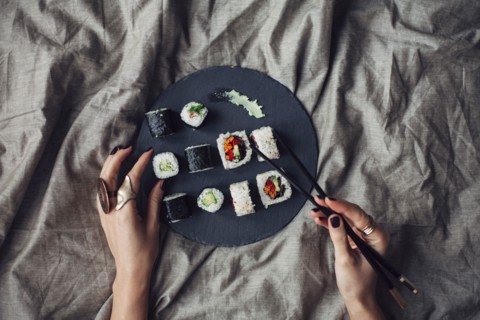 Hands of woman reaching for platter of sushi on bed