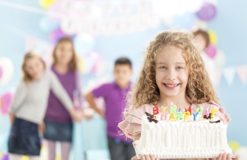 Smiling girl holding birthday cake at party