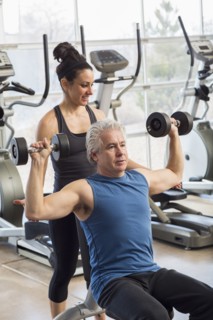 Older Hispanic man working with trainer in gym
