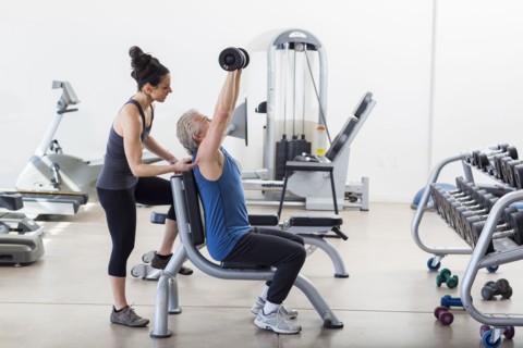 Older Hispanic man working with trainer in gym
