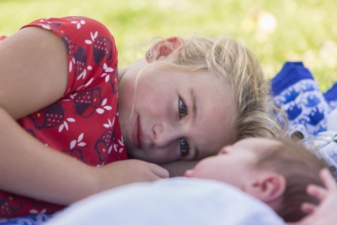 Caucasian girl laying with newborn baby brother