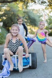 Children in swimsuits pushing cart on rural road