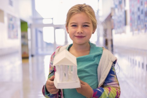 Caucasian girl holding art project in school corridor