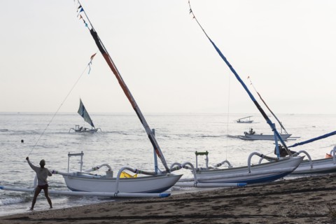 Fisherman pulling sailboat line on beach