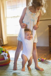 Caucasian girl helping baby walk