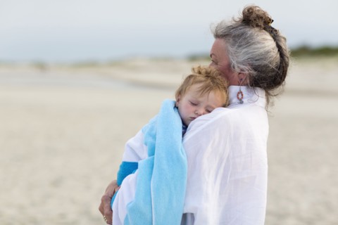 Caucasian woman carrying grandson on beach