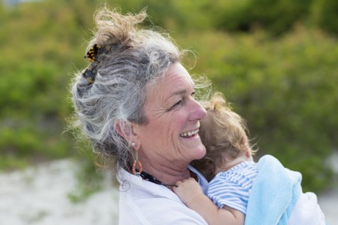 Caucasian woman carrying grandson on beach