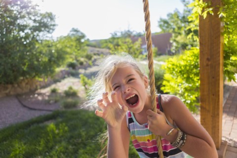 Caucasian girl playing on rope swing